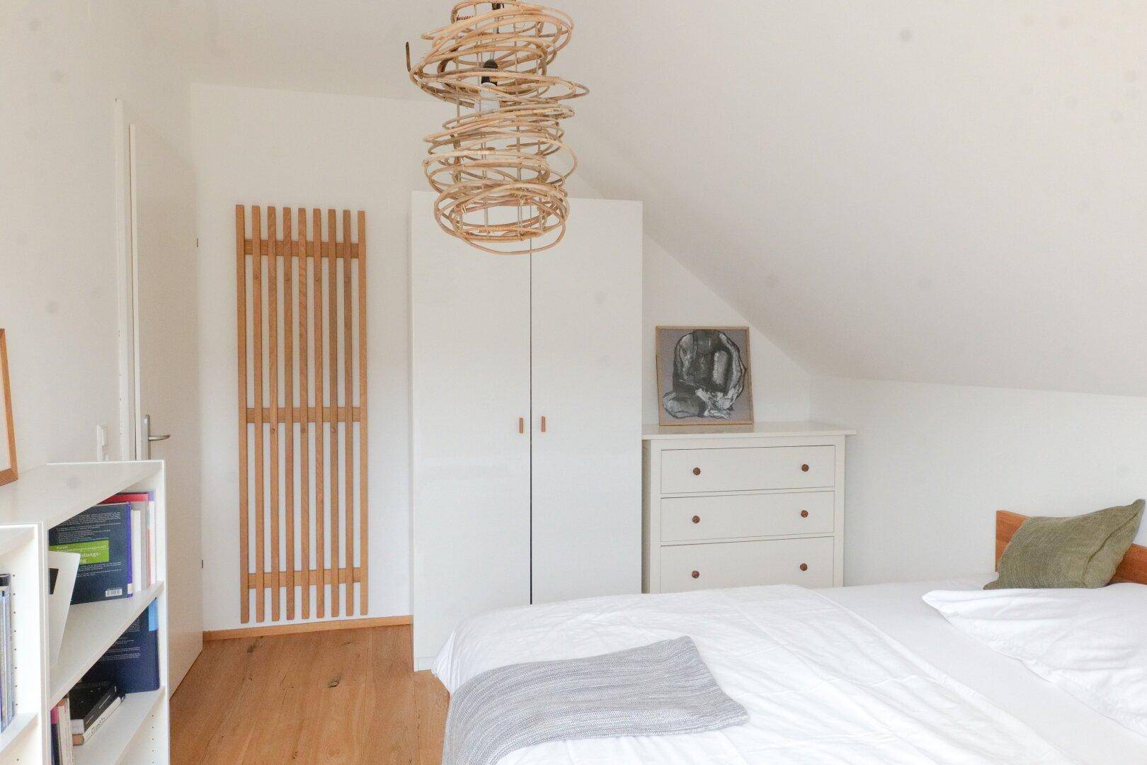 Helles Schlafzimmer mit Holzboden, weißem Kleiderschrank und Dachschräge.