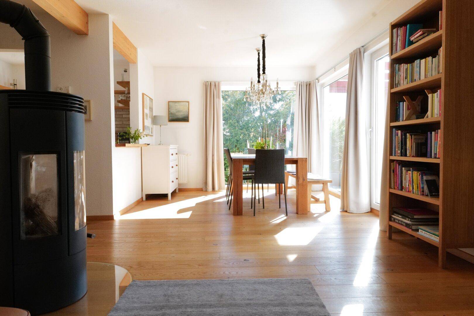 Heller offener Wohn- und Essbereich mit Kaminofen, Holzboden und großen Fenstern zum Garten.