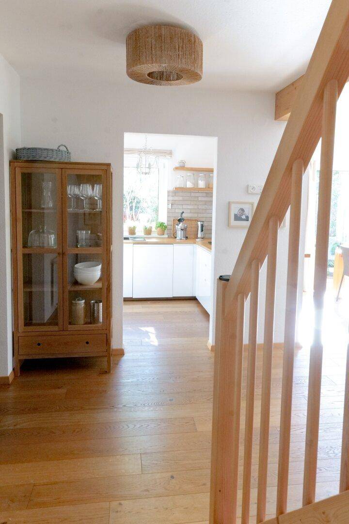 Heller Flur mit Holztreppe, Holzboden und Durchgang zu einer modernen Küche.