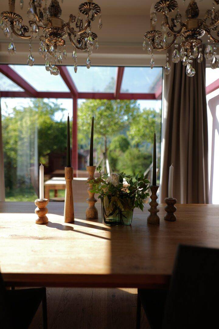 Esstisch mit Kronleuchter und Blick durch große Fenster auf den grünen Garten.