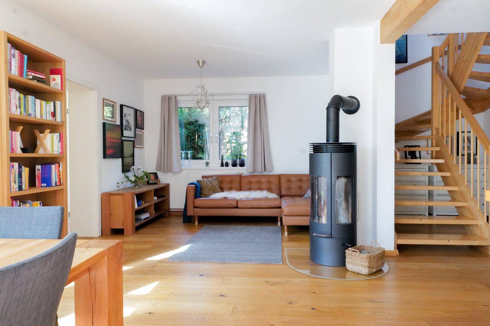 Gemütliches Wohnzimmer mit Kaminofen, Ledersofa, Holzboden und offener Holztreppe.