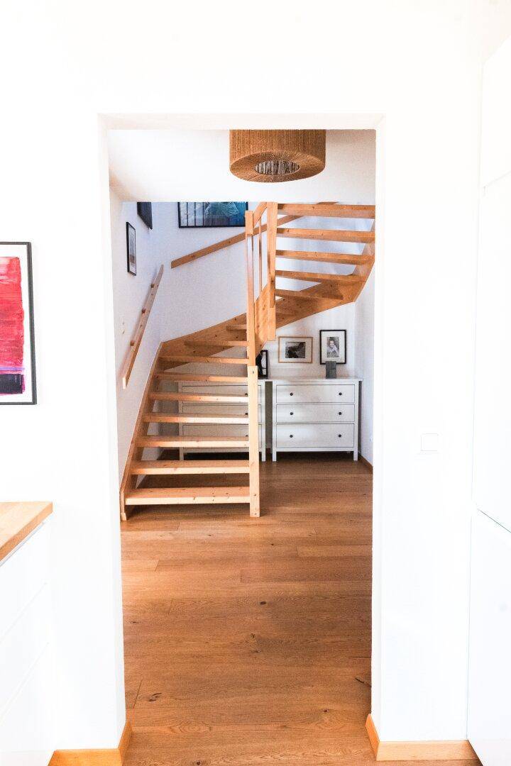 Heller Flur mit geschwungener Holztreppe, Holzboden und weißer Kommode.