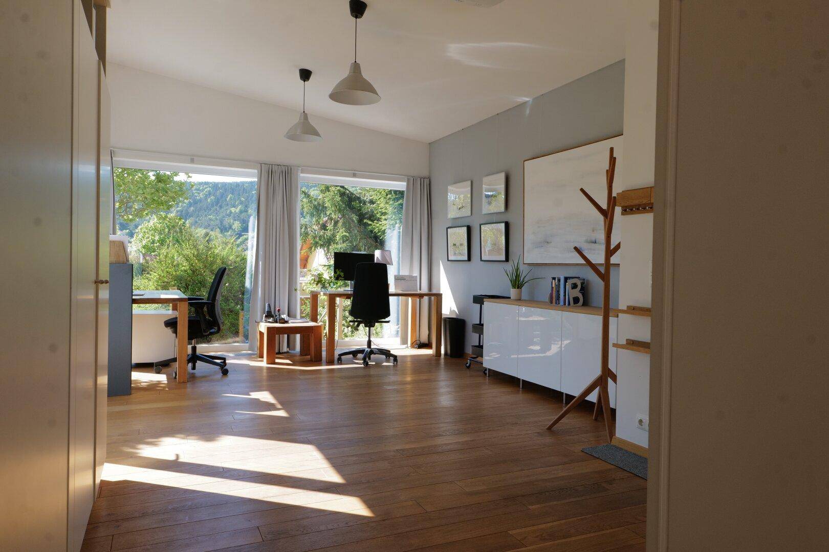 Helles Arbeitszimmer mit Holzboden, großen Fenstern und Blick ins Grüne.