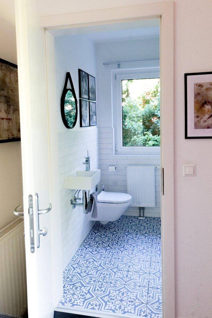 Modernes Gäste-WC mit Fenster, Wand-WC und auffälligen blauen Bodenfliesen.