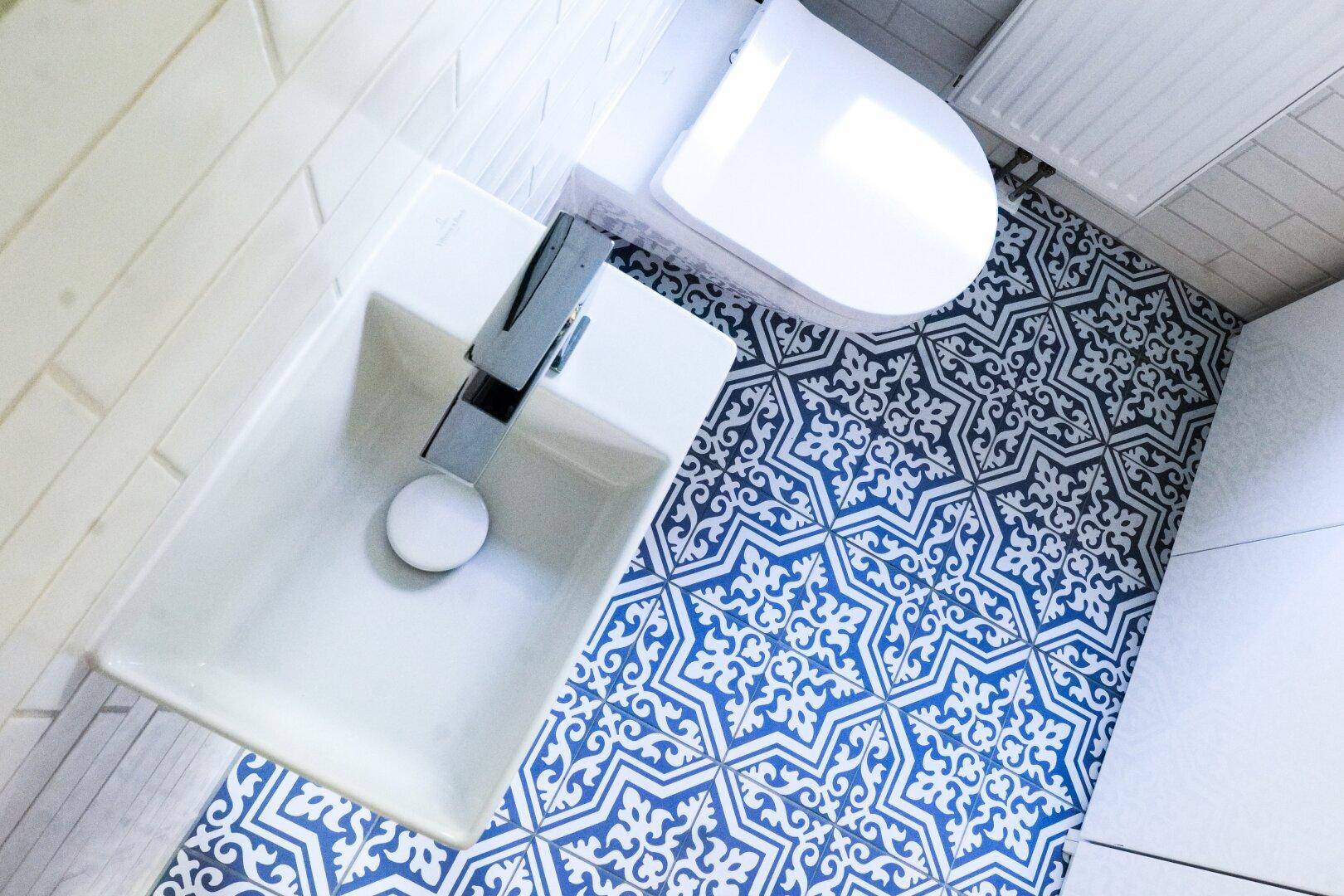 Nahaufnahme des Gäste-WCs mit Wand-WC, kleinem Waschbecken und gemusterten Bodenfliesen.