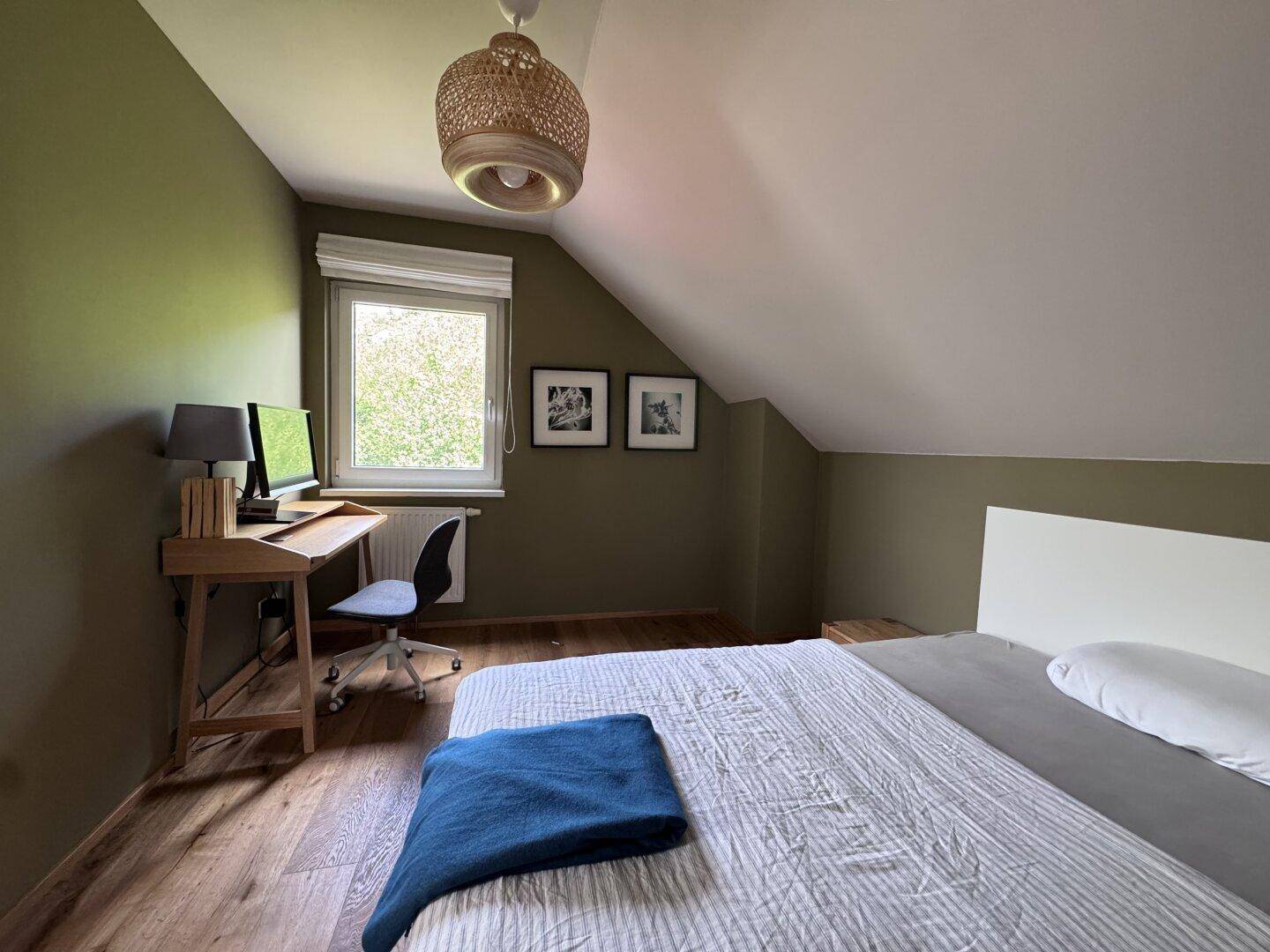 Schlafzimmer mit Holzboden, Schreibtisch, grünen Wänden und Dachschräge.