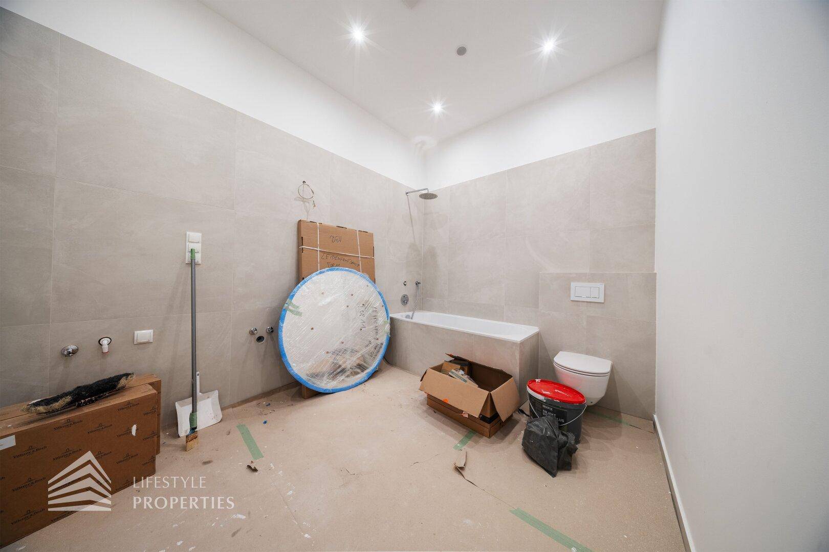Badezimmer im Bau mit Badewanne, Wand-WC und modernen Fliesen, bereit zur Fertigstellung.