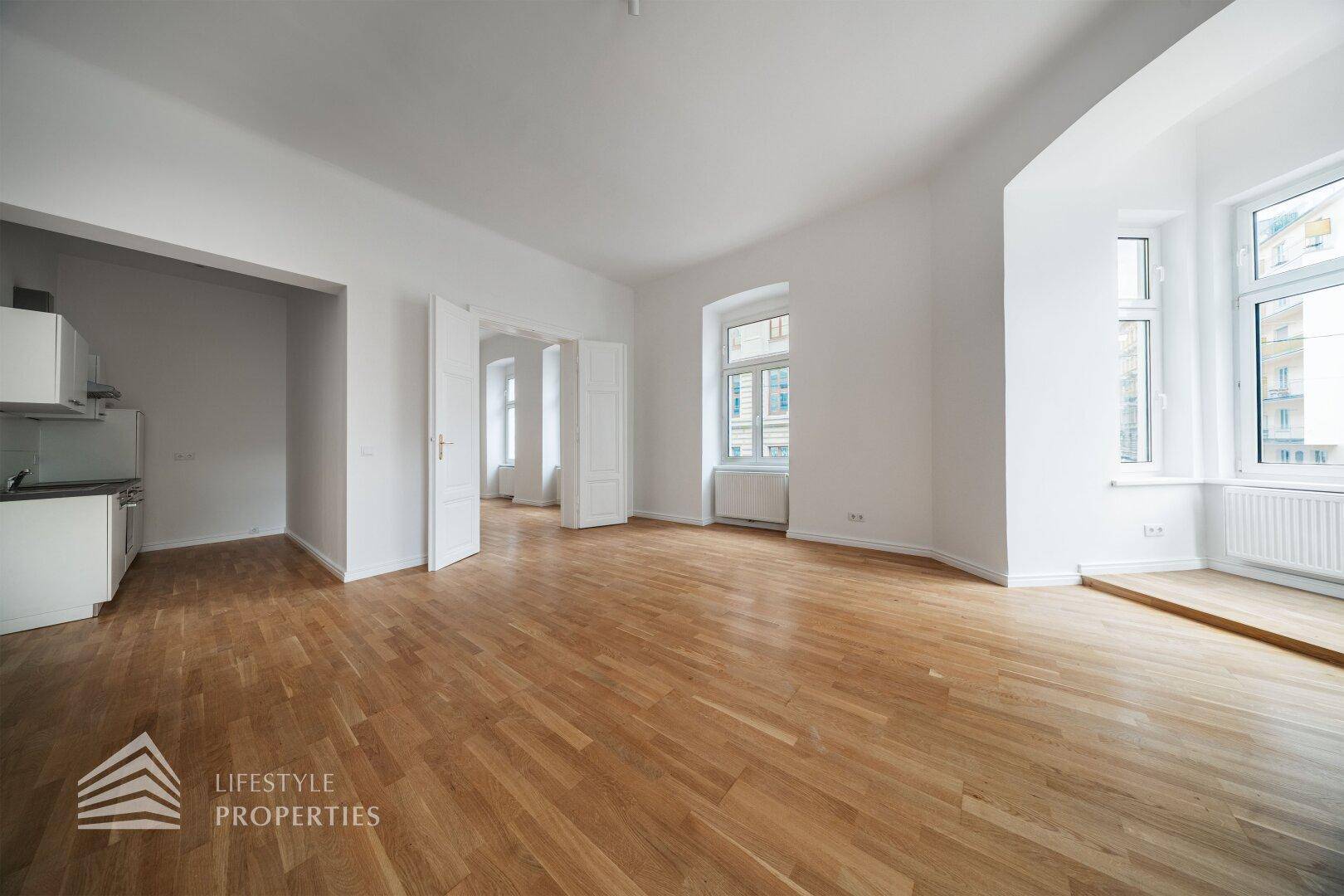 Offener Wohnbereich mit Parkettboden und Zugang zu einer angrenzenden Küchennische.