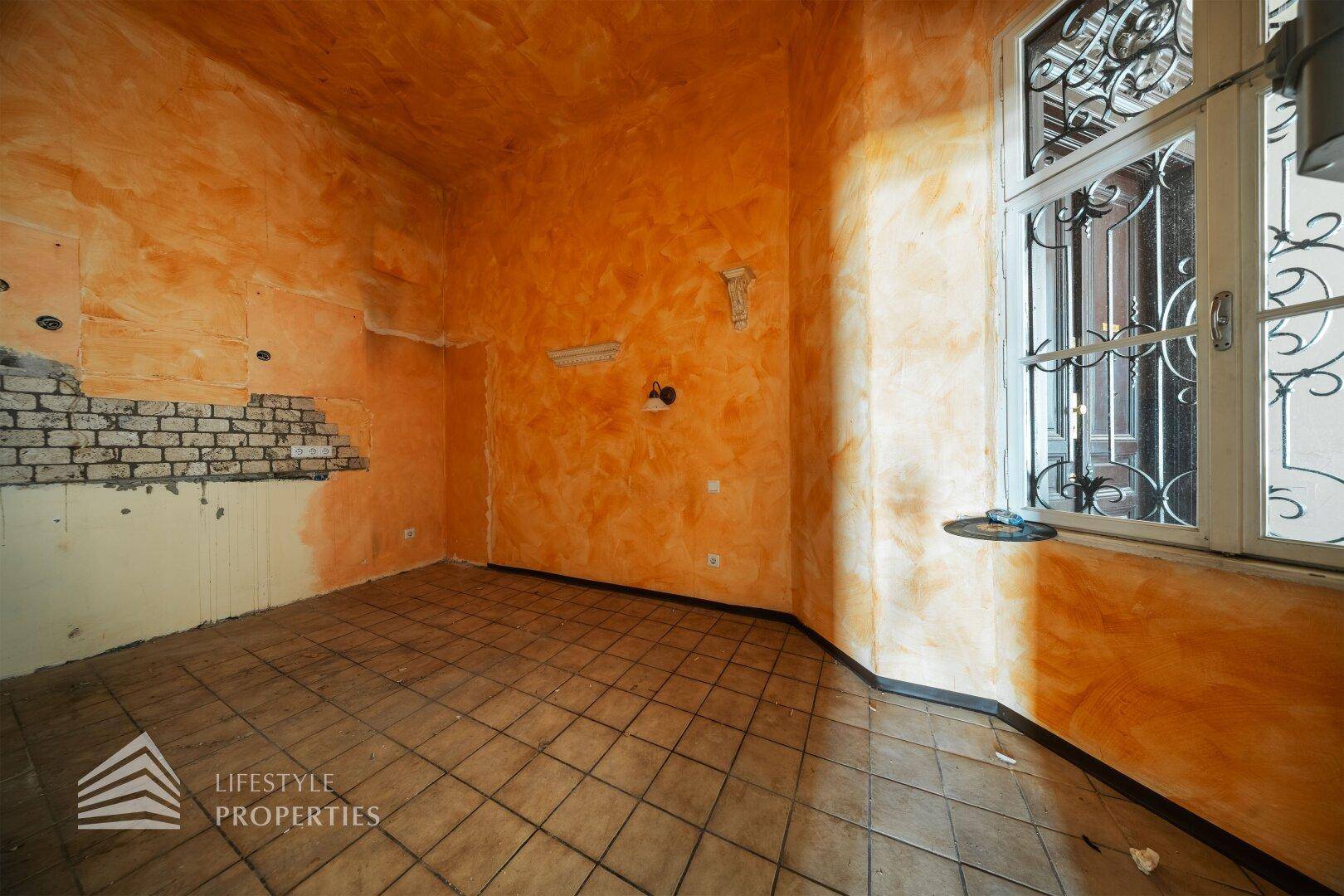 Raum mit orangefarbenen Wänden und Fliesenboden, bereit für eine neue Kücheninstallation.