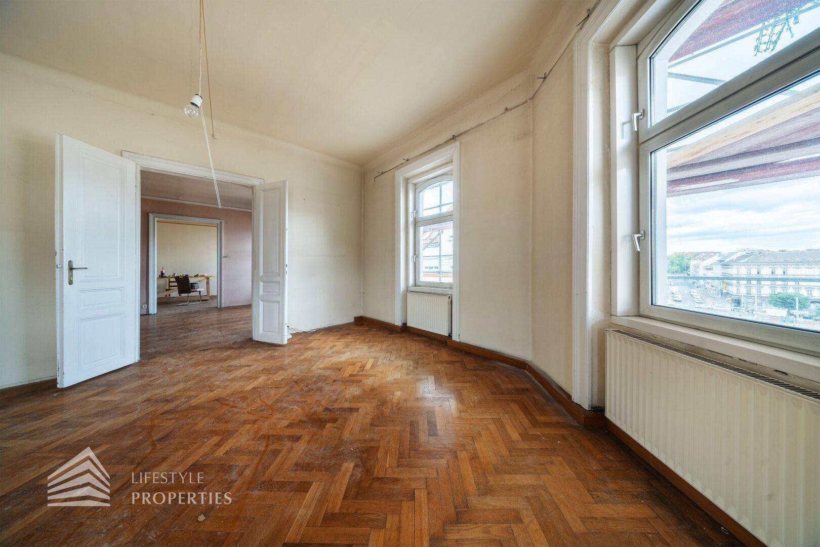 Lichtdurchflutetes Zimmer mit Fischgrätparkett und großen Fenstern, die einen weiten Blick bieten.