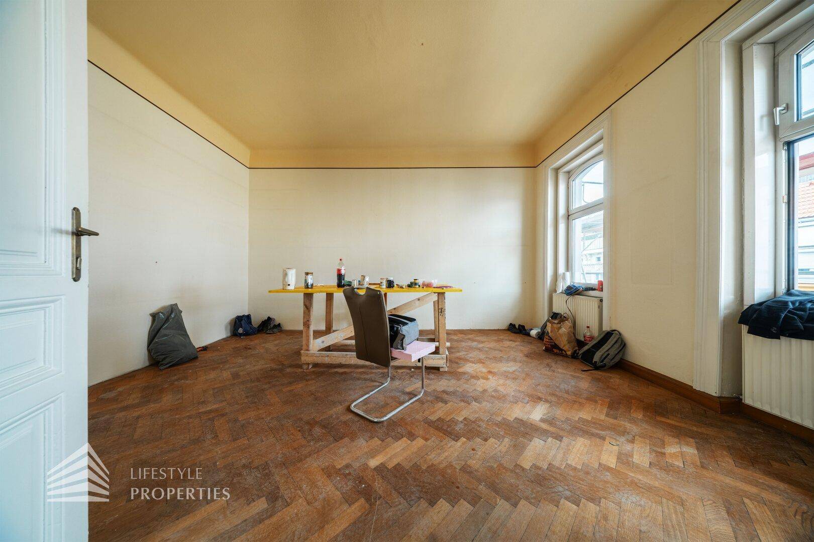 Helles Zimmer mit Fischgrätparkett und hohen Decken, bietet viel Platz für individuelle Einrichtung.