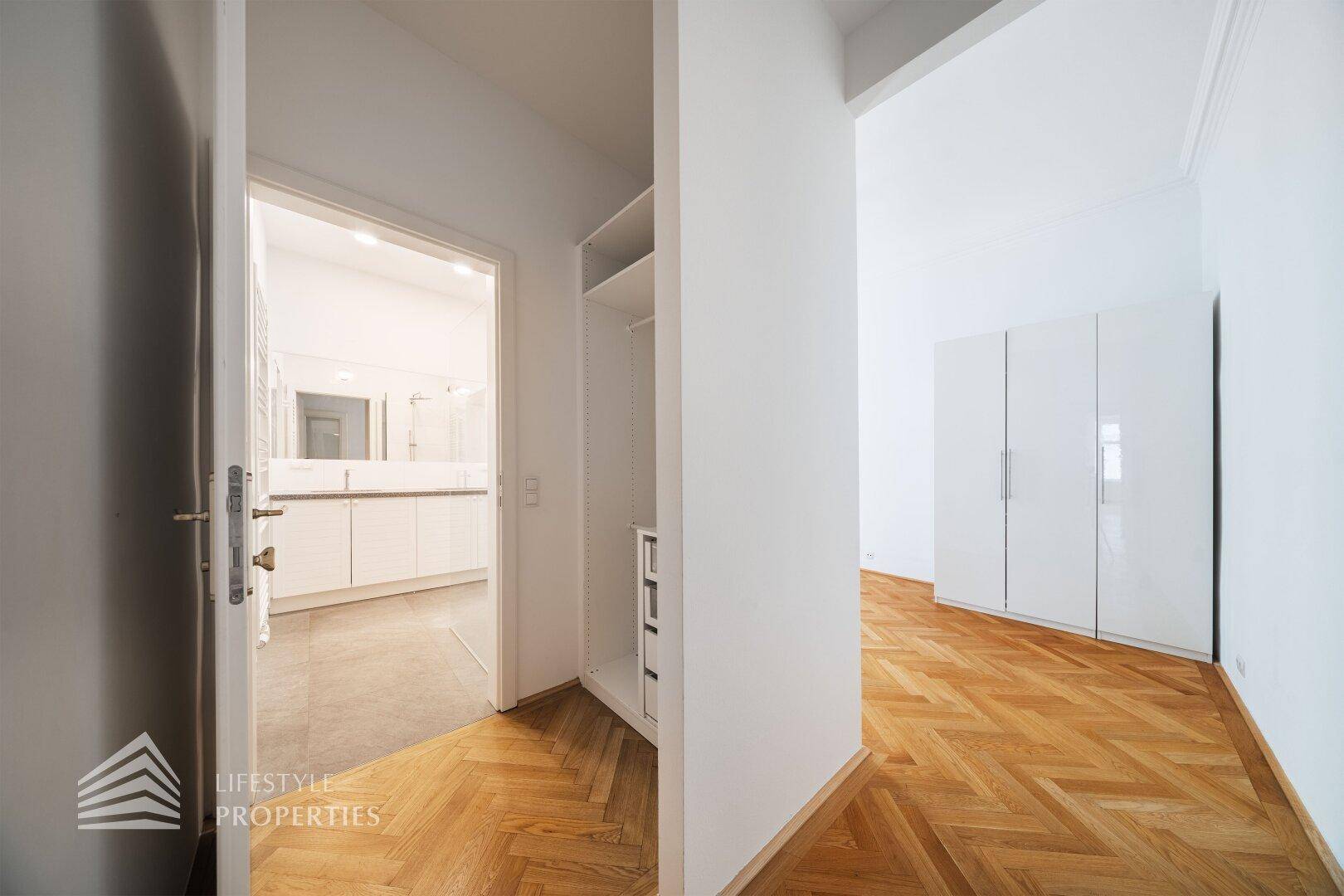 Flur mit Fischgrätparkett und integriertem Regal, der zu einem Badezimmer führt.