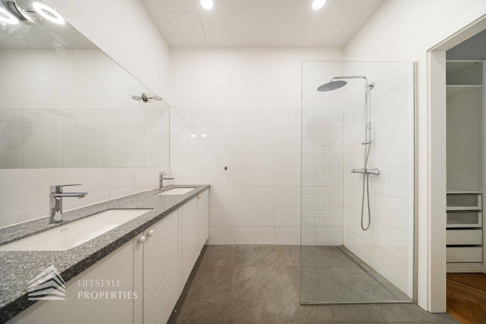 Modernes Badezimmer mit großer begehbarer Dusche, Doppelwaschbecken und Fliesenboden.