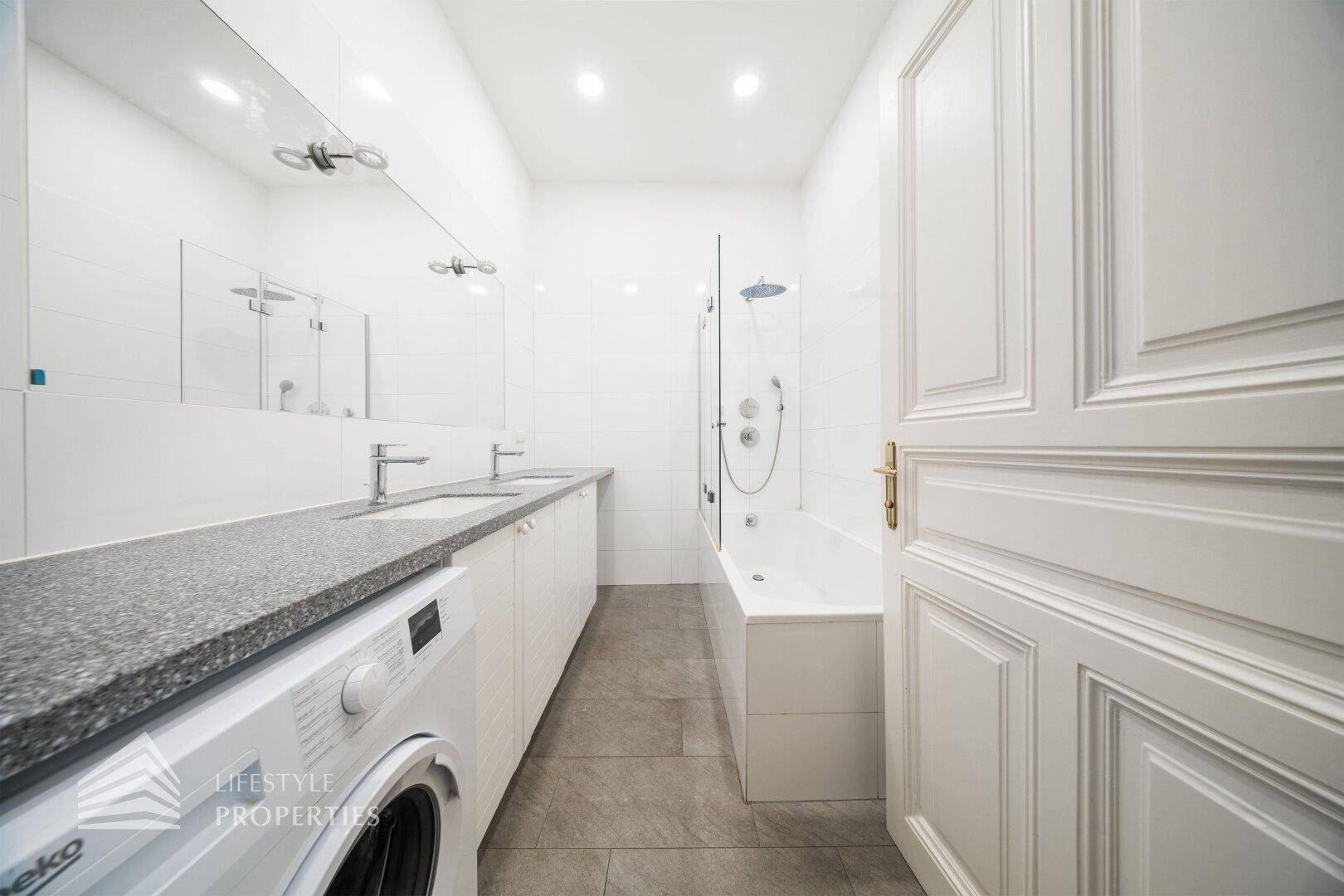 Modernes Badezimmer mit Doppelwaschbecken, Badewanne mit Duschfunktion und Waschmaschine.