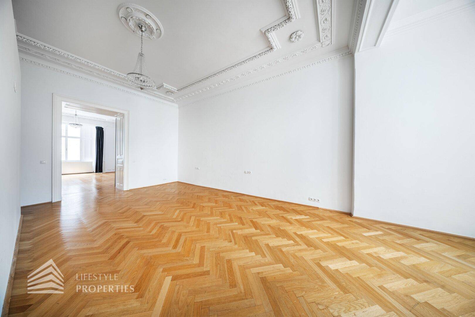 Großes, helles Wohnzimmer mit Fischgrätparkett und Stuckdecken, das viel Platz bietet.