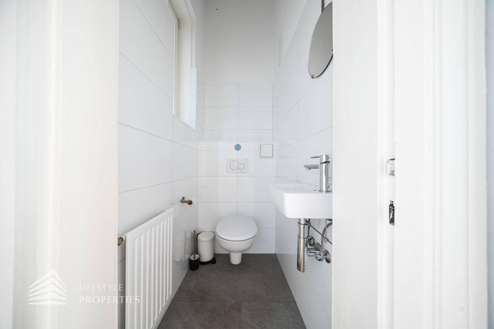 Helles Gäste-WC mit Fenster, Heizung und modernem Waschbecken, in weiß gefliest.