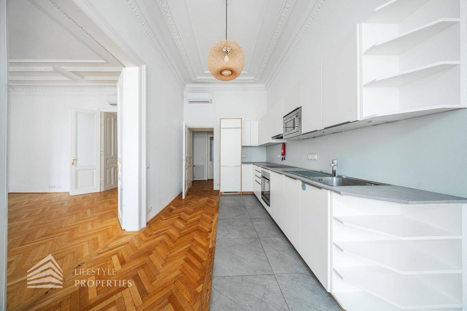 Moderne Einbauküche mit weißen Schränken, grauen Fliesen und Holzparkett im angrenzenden Bereich.