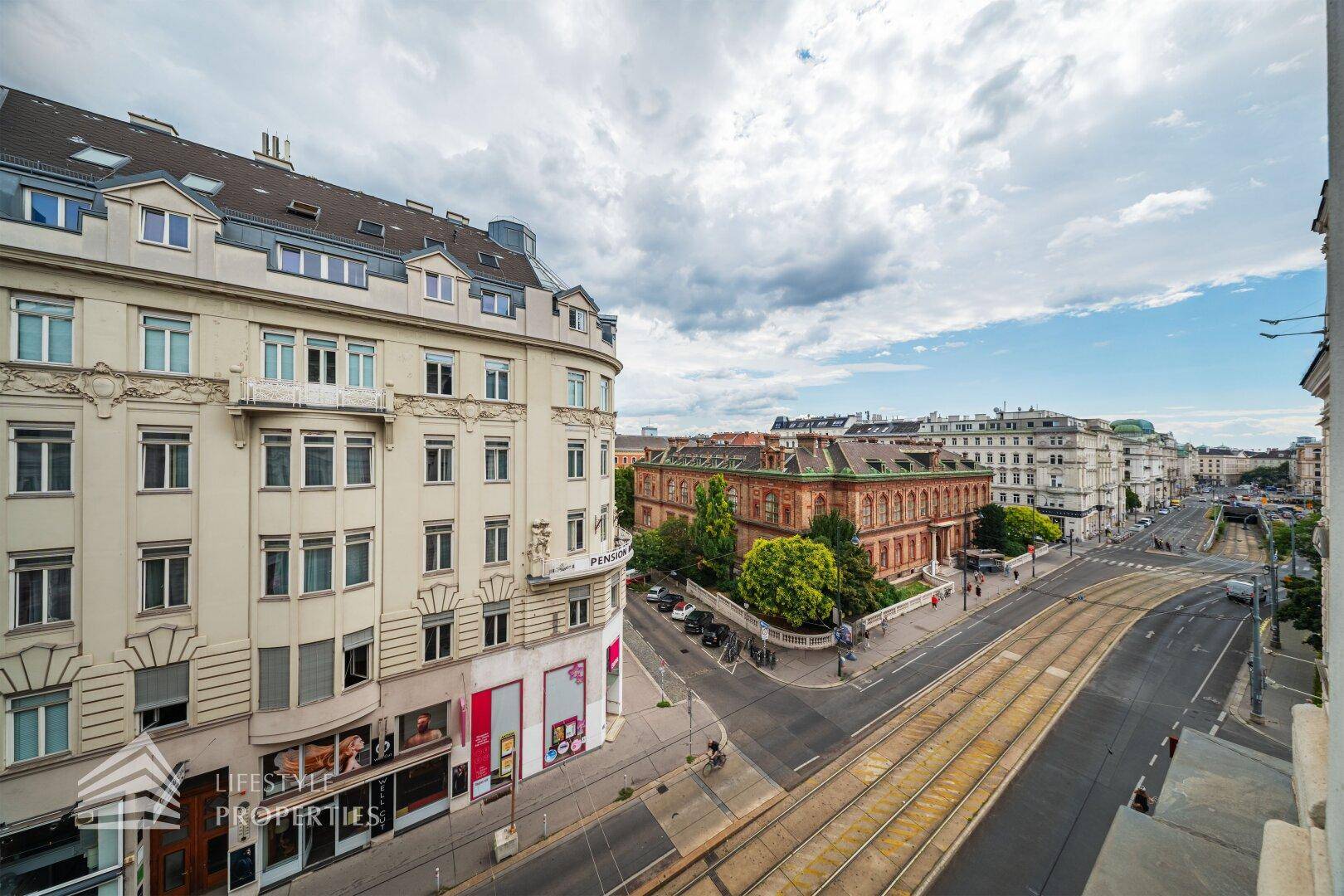 Weitläufiger Blick über eine belebte Stadtstraße mit historischen Gebäuden und Straßenbahnschienen.
