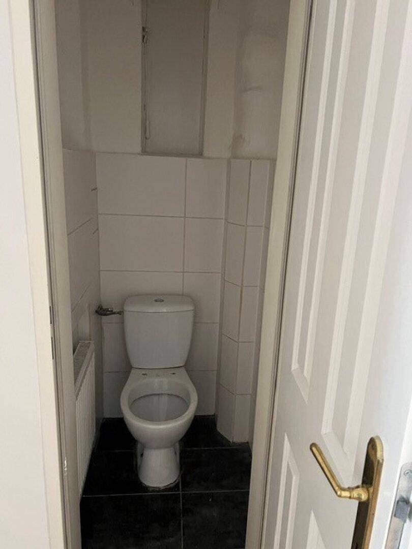 Kompaktes WC mit weißer Toilette und Fliesen an den Wänden und auf dem Boden.