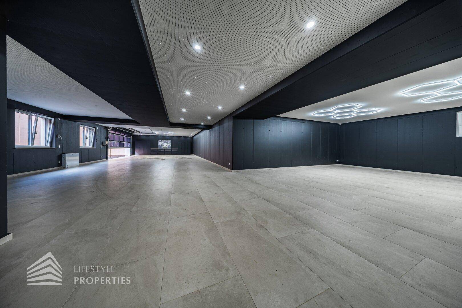 Weitläufiger Garagenraum mit moderner Beleuchtung, dunklen Wänden und großem Rolltor.