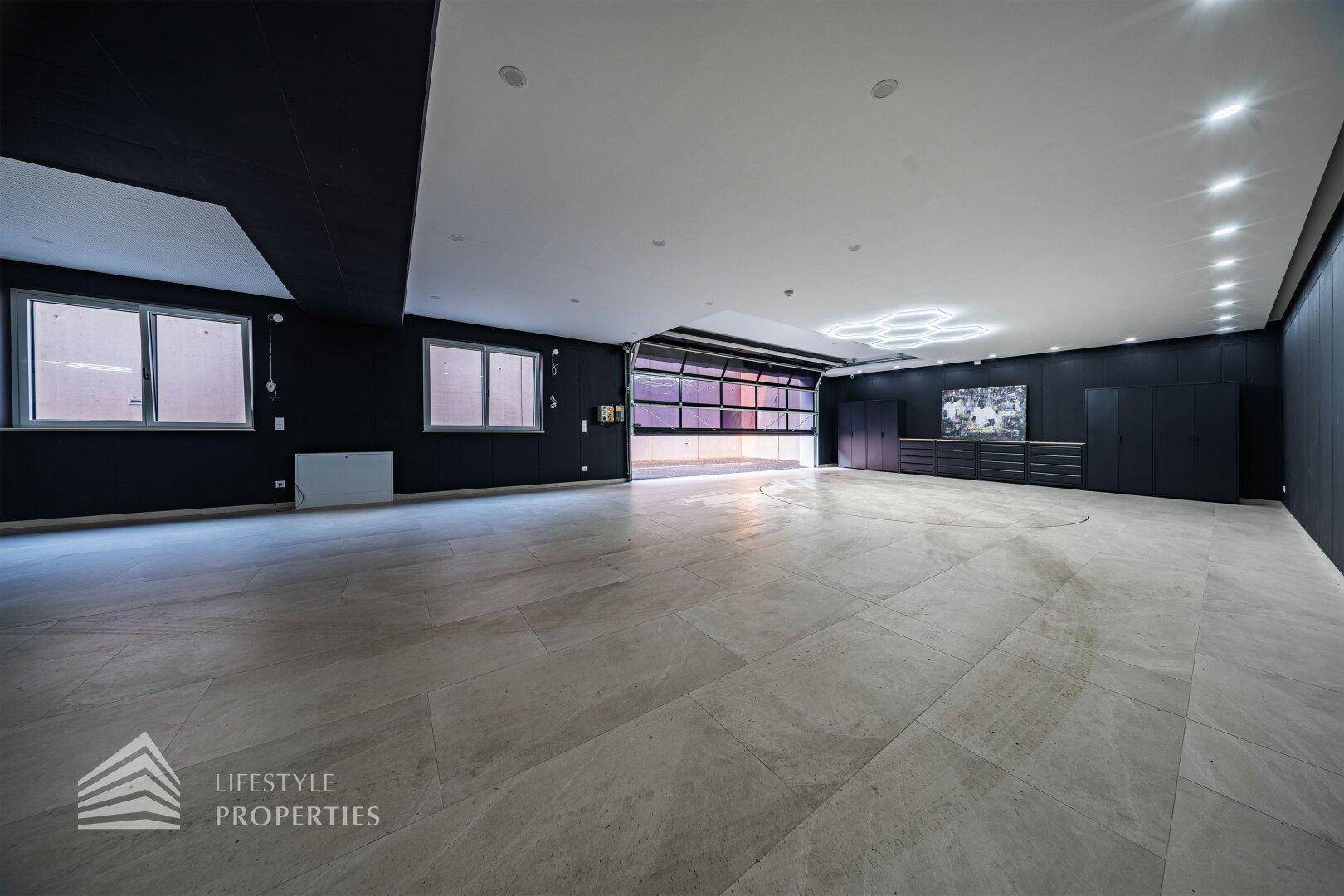Heller Garagenraum mit großen Fenstern, modernem Rolltor und stilvoller Deckenbeleuchtung.