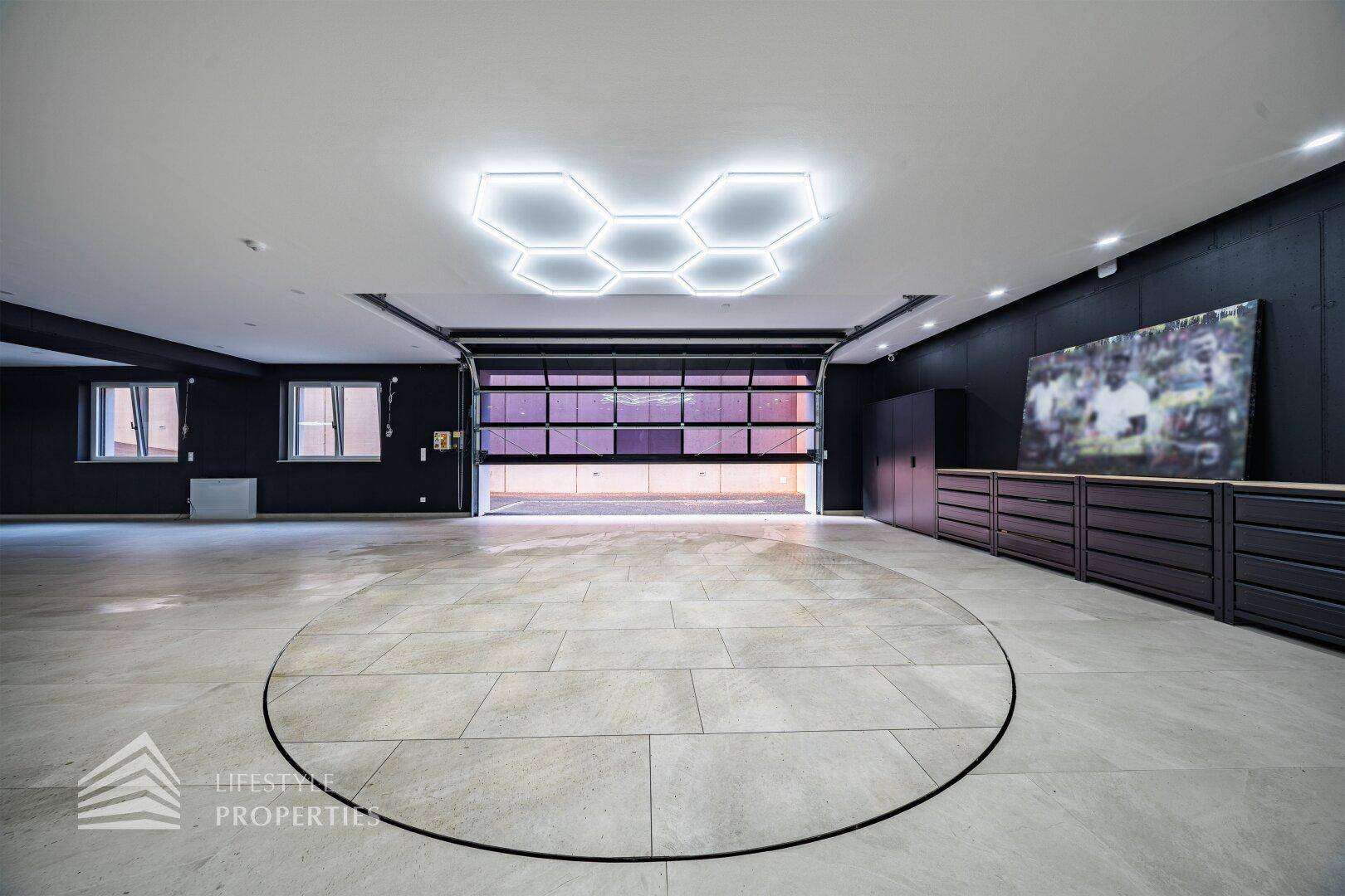 Große Garage mit Rolltor, Fliesenboden und futuristischer Deckenbeleuchtung in Wabenform.