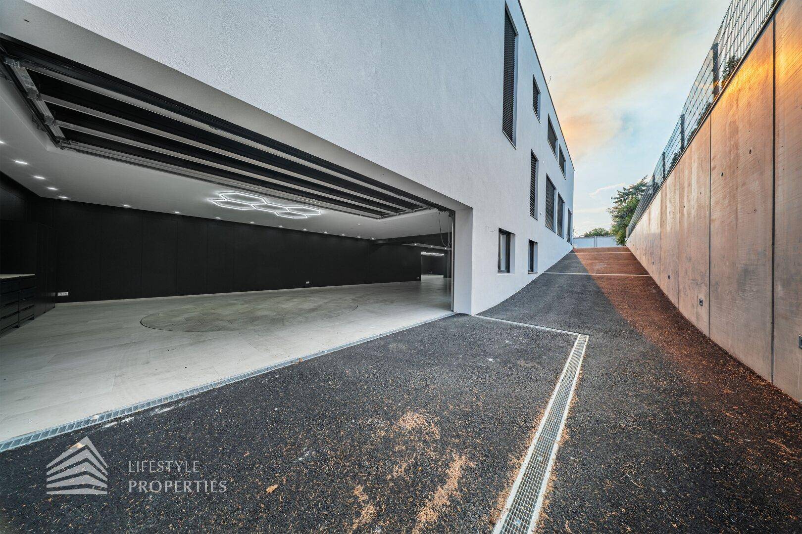 Moderne Gebäudefassade mit offener Garage und Zufahrt zu einem unterirdischen Bereich.