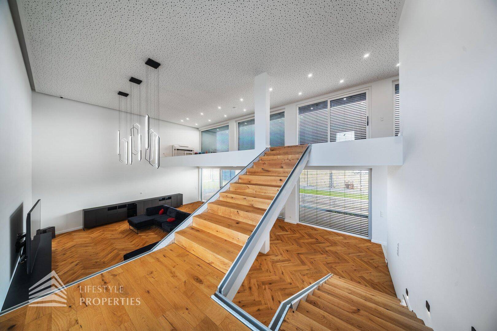 Heller Wohnbereich mit offener Holztreppe, hohen Decken und modernen Pendelleuchten.
