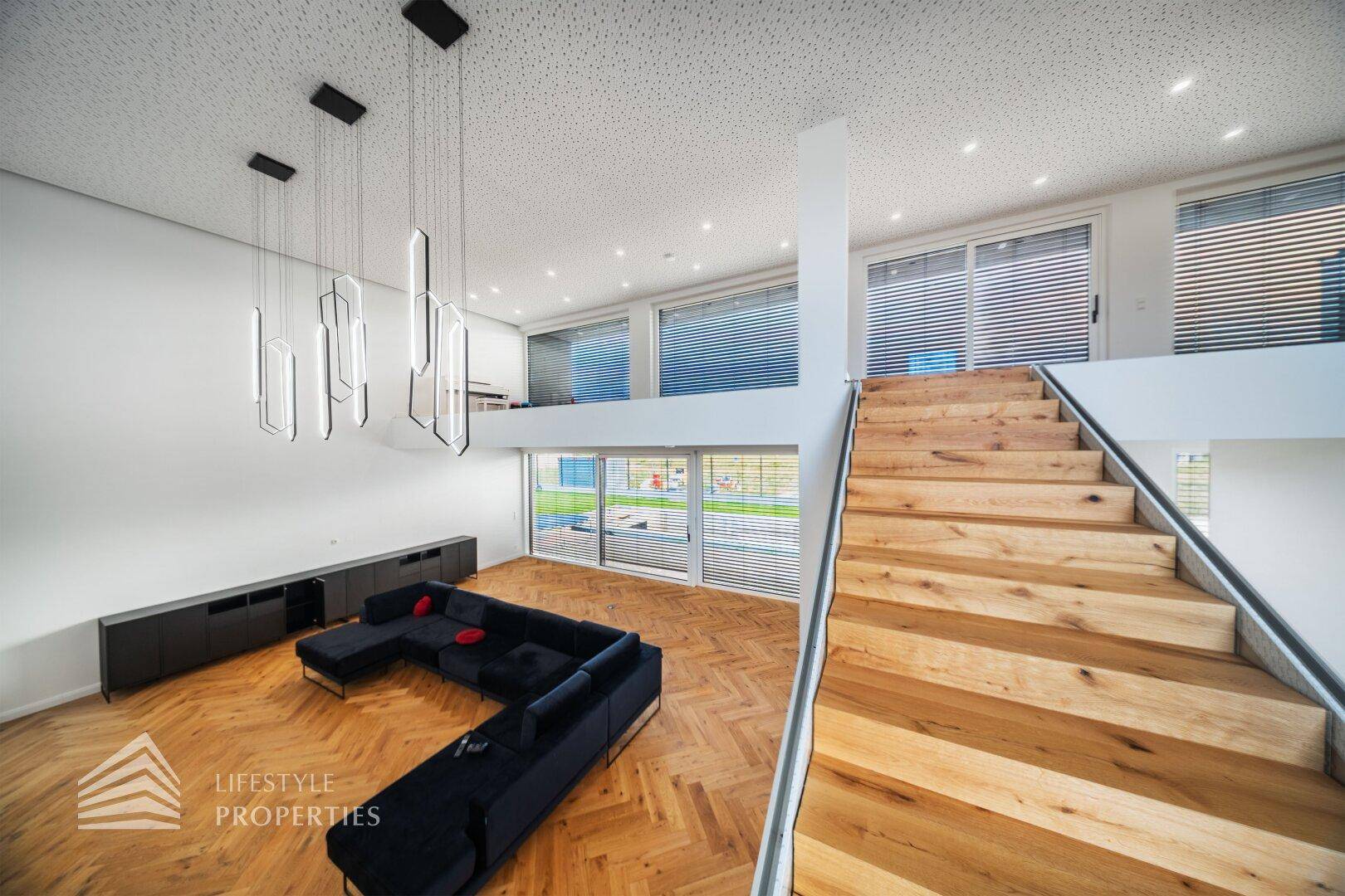 Offener Wohnbereich mit Holztreppe, hohen Decken und Blick auf den Außenbereich.