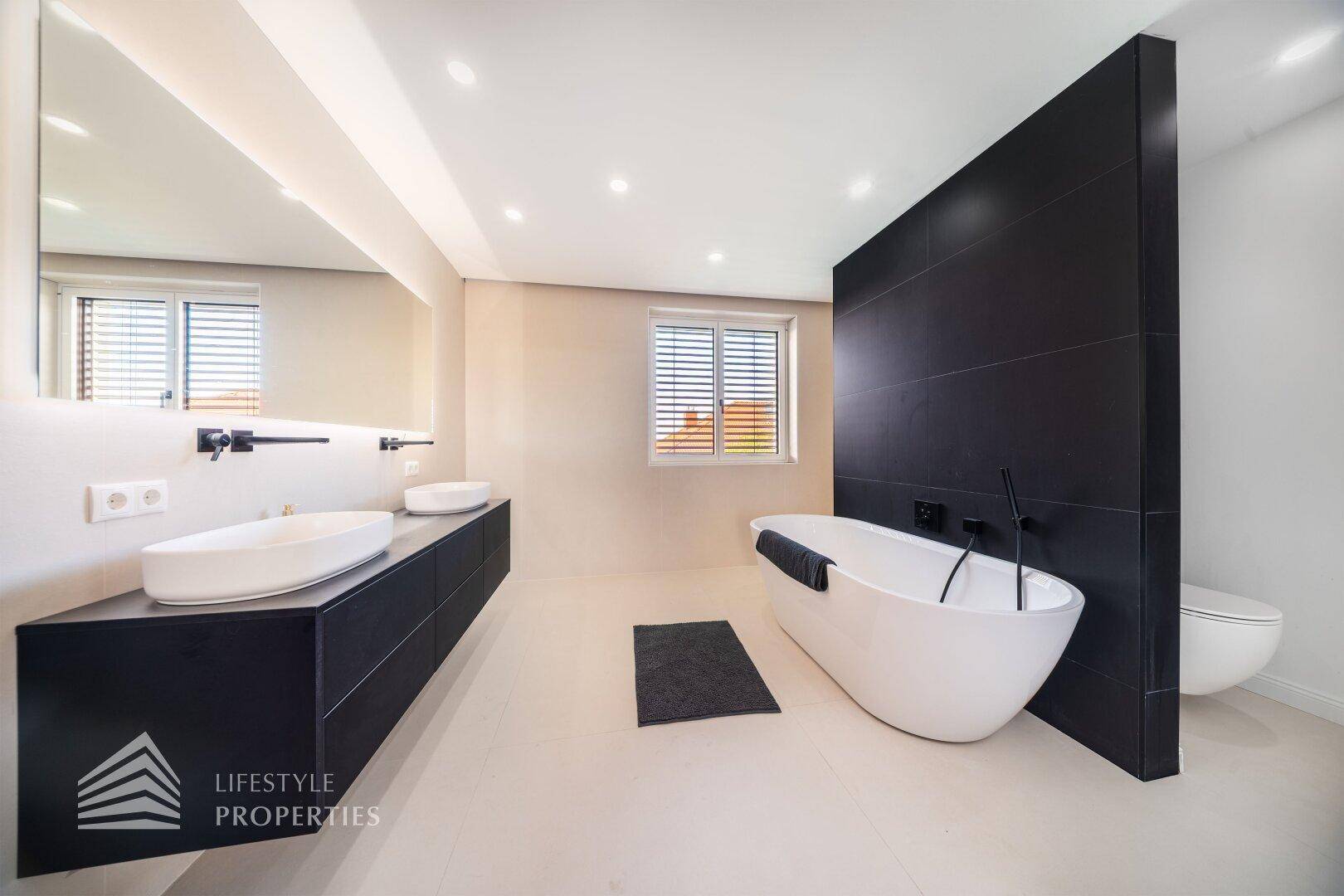Modernes Badezimmer mit freistehender Badewanne, Doppelwaschbecken und schwarzen Akzenten.
