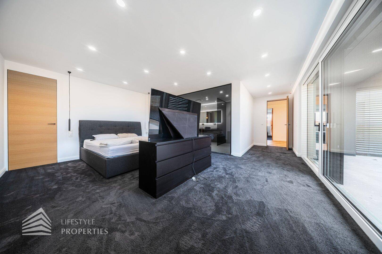 Modernes Schlafzimmer mit Teppichboden, großem Bett und Zugang zum luxuriösen Badezimmer.