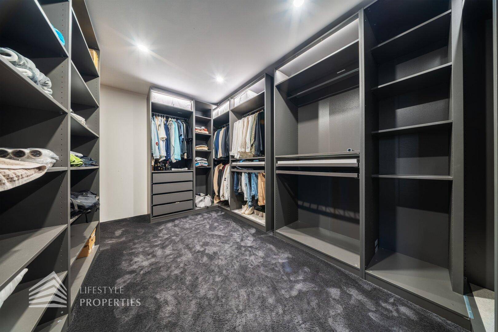 Geräumiger begehbarer Kleiderschrank mit modernen grauen Regalsystemen und Teppichboden.