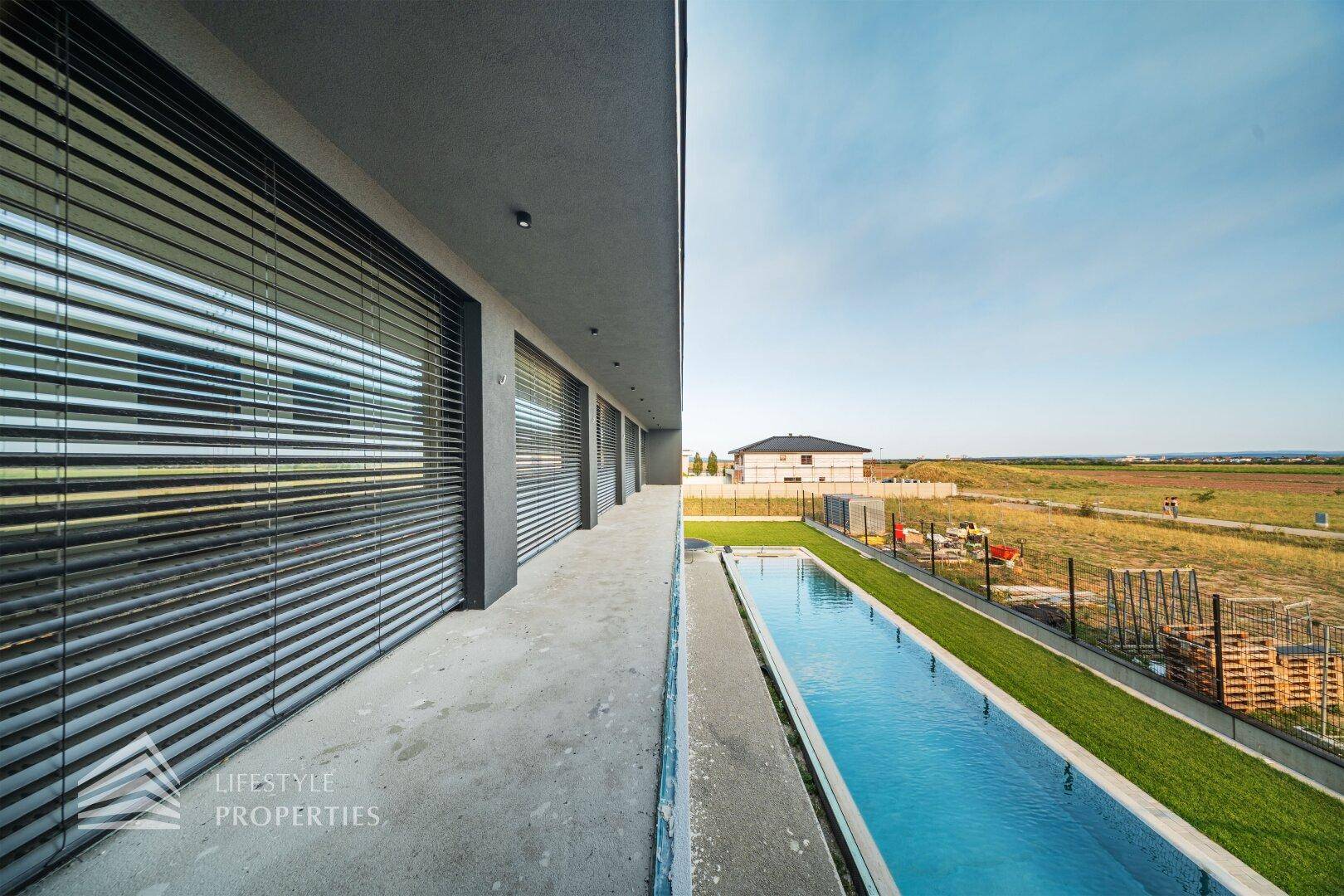 Moderne Hausfassade mit vielen Fenstern, Jalousien und einem langen, eleganten Swimmingpool.