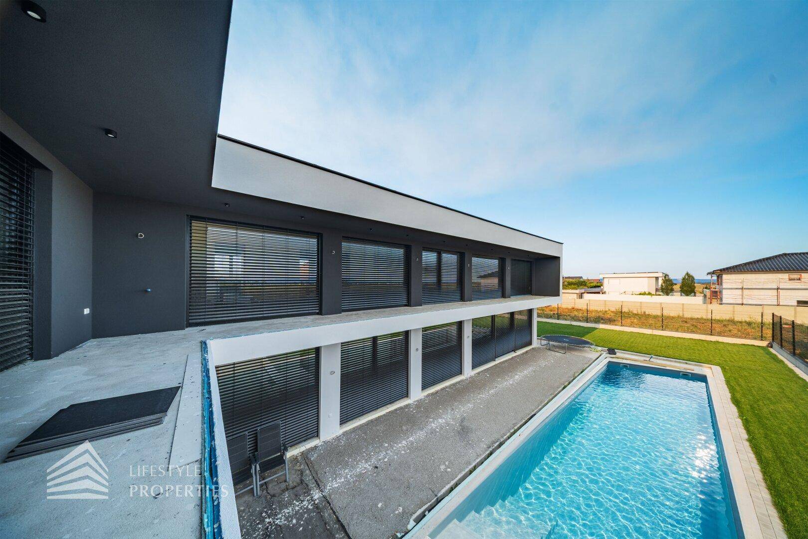 Moderne Architektur mit langem Pool und Balkon im Obergeschoss, umgeben von Natur.
