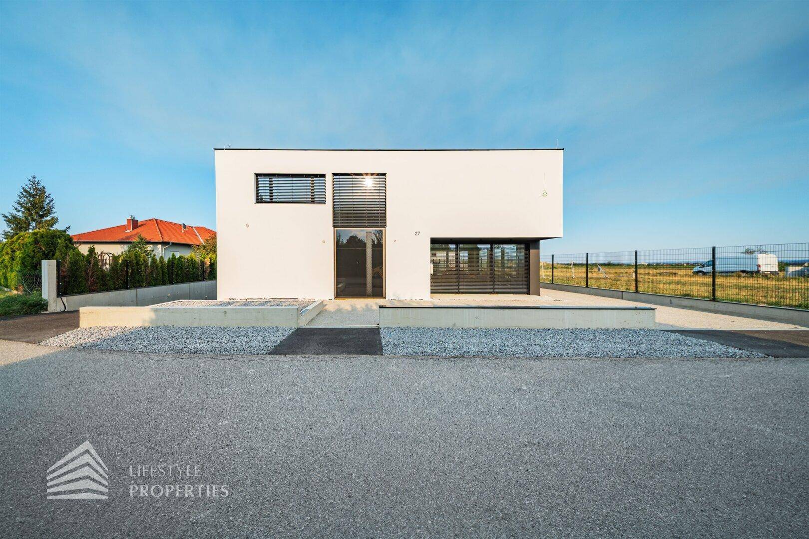 Frontansicht des modernen, würfelförmigen Hauses mit weißer Fassade und klaren Linien.