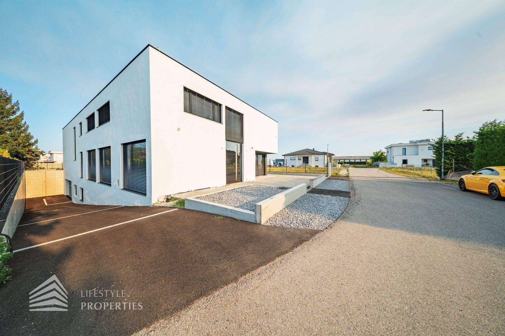 Seitenansicht des modernen Hauses mit Zufahrt, Eingangsbereich und minimalistischer Gestaltung.