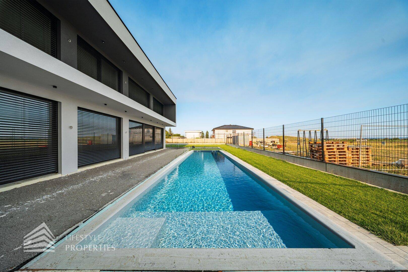 Langer, schmaler Pool neben der modernen Villa mit Rasenfläche und Blick auf die Umgebung.