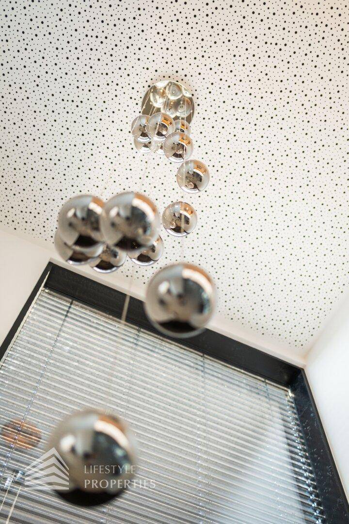 Moderne Decke mit perforierter Oberfläche und stilvoller Hängeleuchte über einem Fenster.