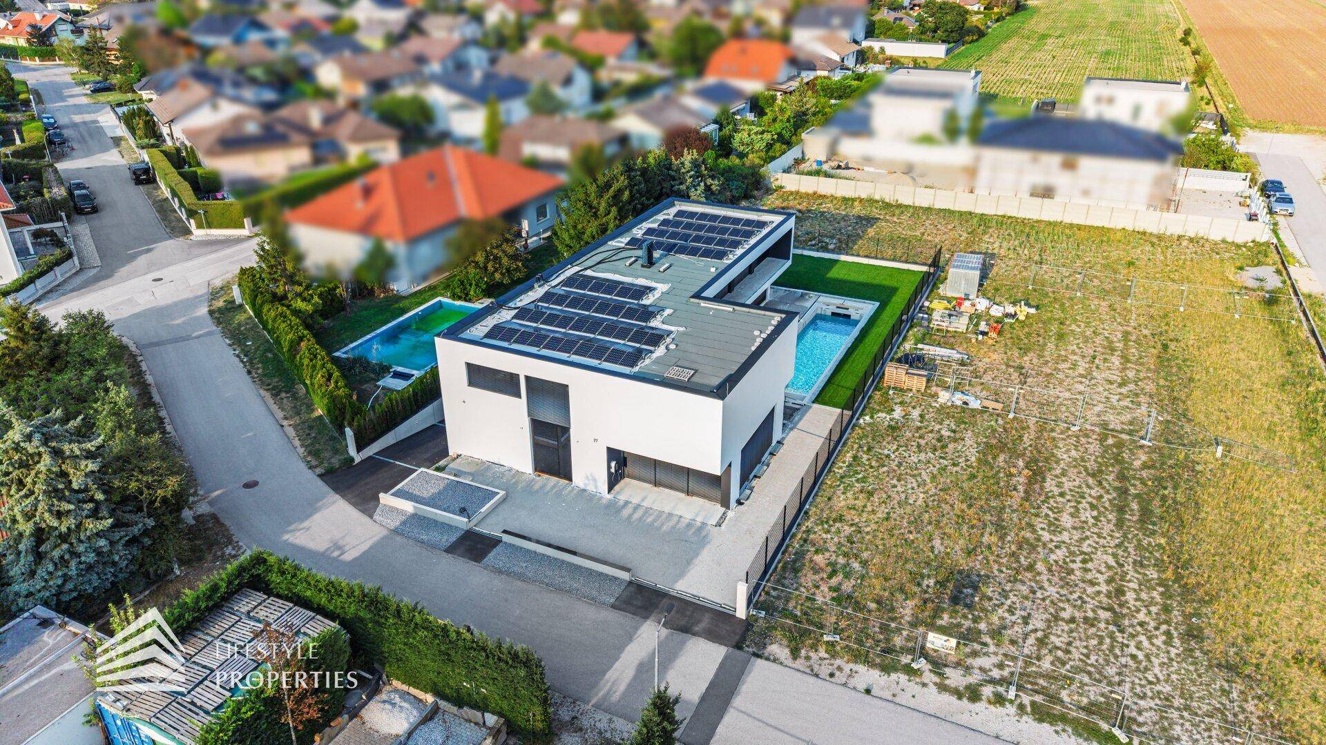 Moderne Villa mit Photovoltaikanlage und Pool, umgeben von Wohnbebauung und Grünflächen.