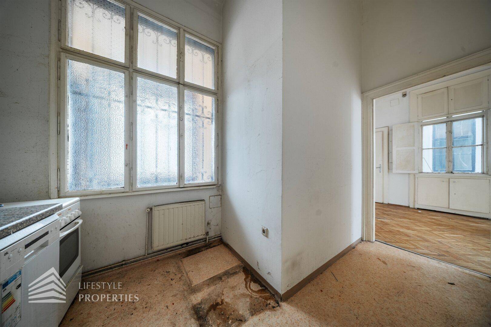 Einfache Küche mit Fenster, Spüle und Herd, die eine umfassende Modernisierung erfordert.