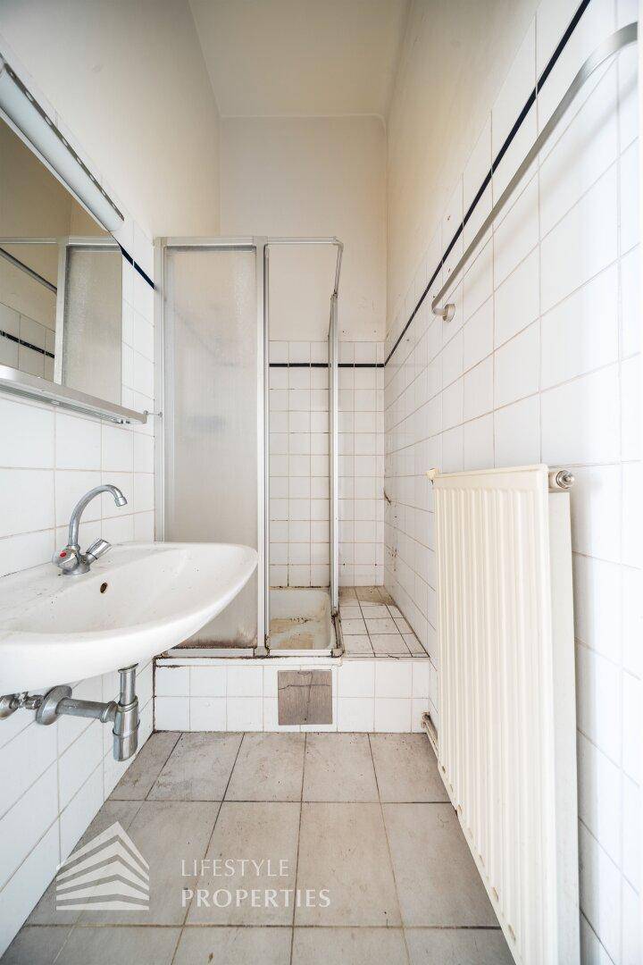Gefliestes Badezimmer mit Dusche und Waschbecken, in einfachem, aber funktionsfähigem Zustand.