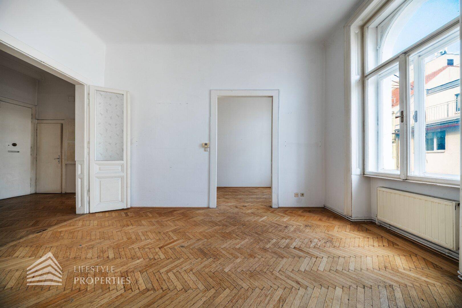 Heller Raum mit Fischgrätparkett, hohen Fenstern und Zugang zu angrenzenden Zimmern, typisch für Altbau.