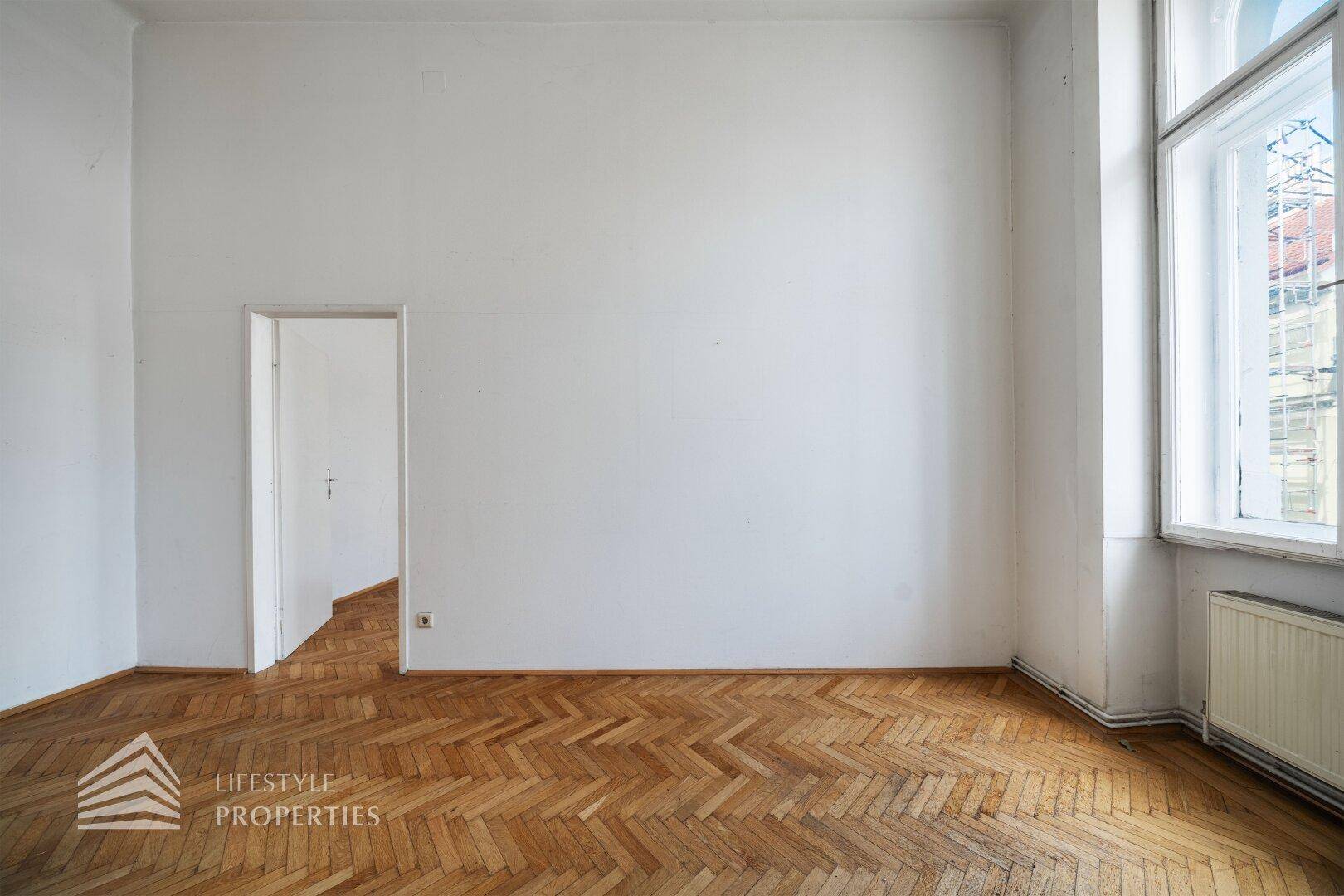 Geräumiges Zimmer mit hohen Wänden, Fischgrätparkett und einem großen Fenster, bereit zur individuellen Gestaltung.