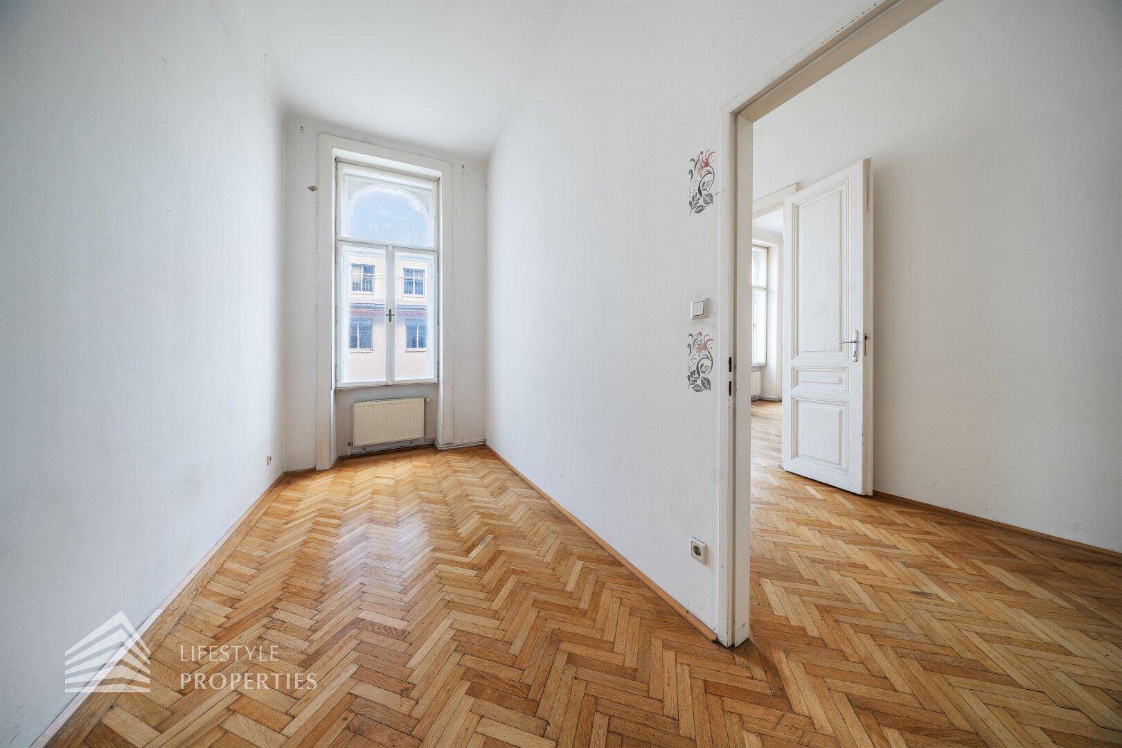 Kleineres Zimmer mit Fischgrätparkett und einem hohen Bogenfenster, ideal als Schlaf- oder Arbeitszimmer.