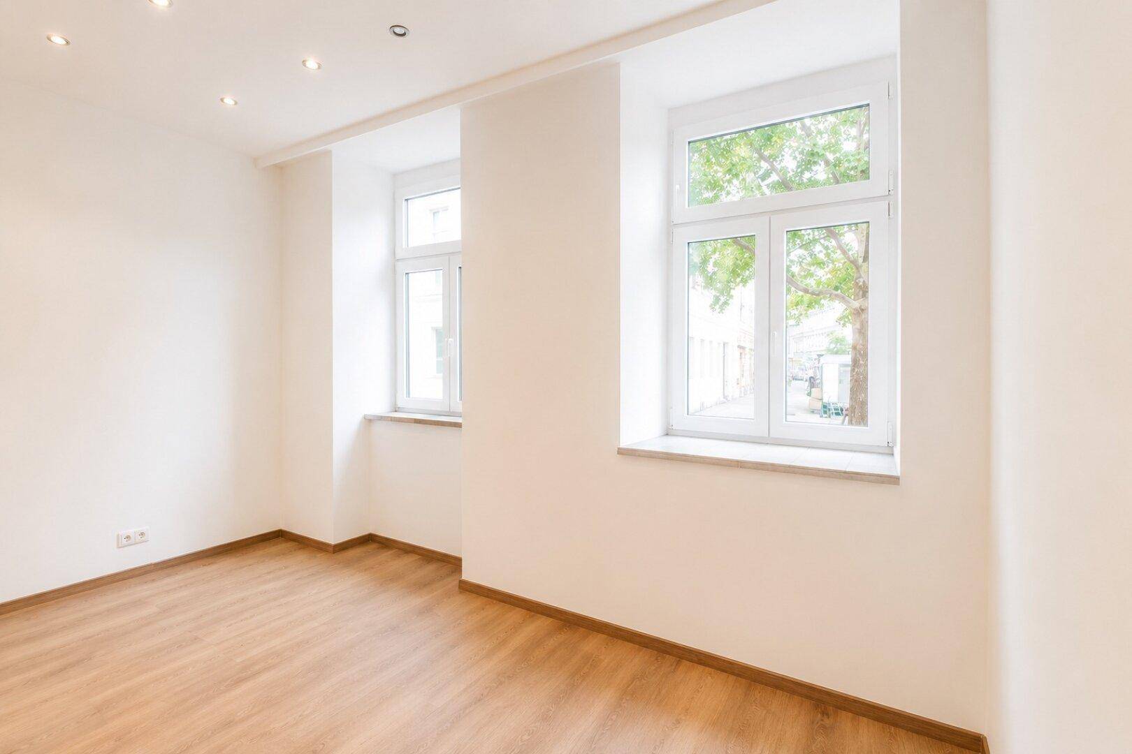 Nahaufnahme der Fenster in einem hellen Raum mit Holzboden und Blick auf Bäume im Freien.