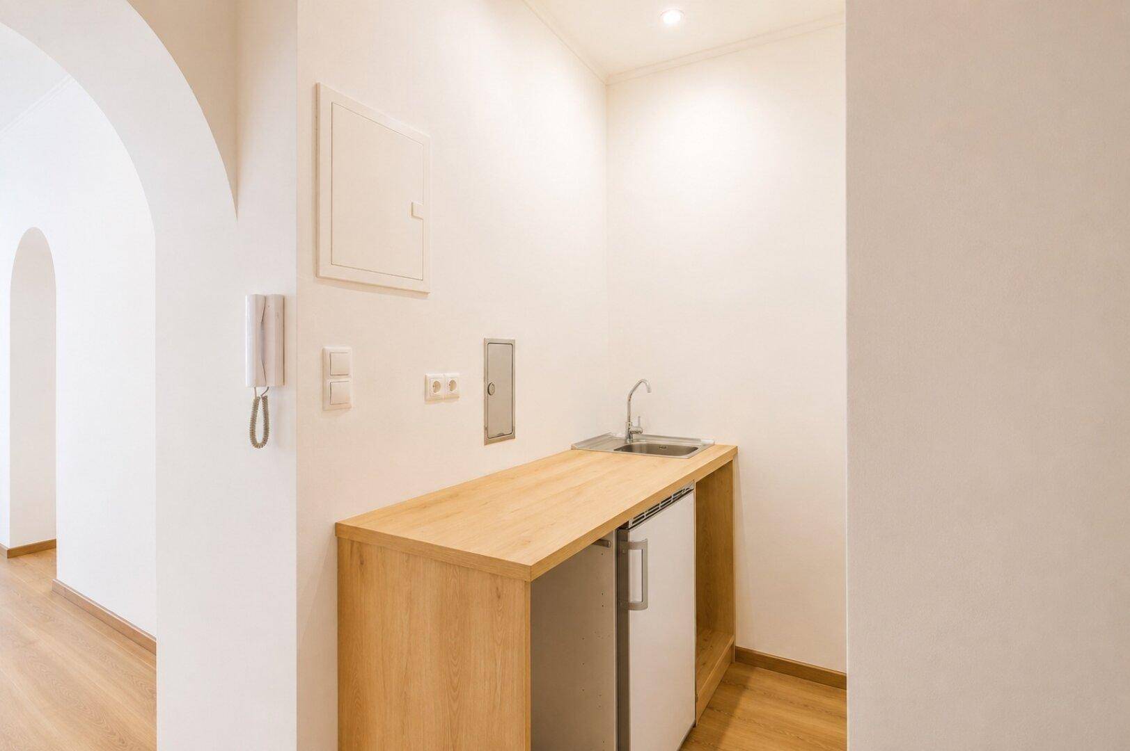 Detailansicht der Küchenzeile mit Spüle, Armatur, Kühlschrank und heller Holzarbeitsplatte.