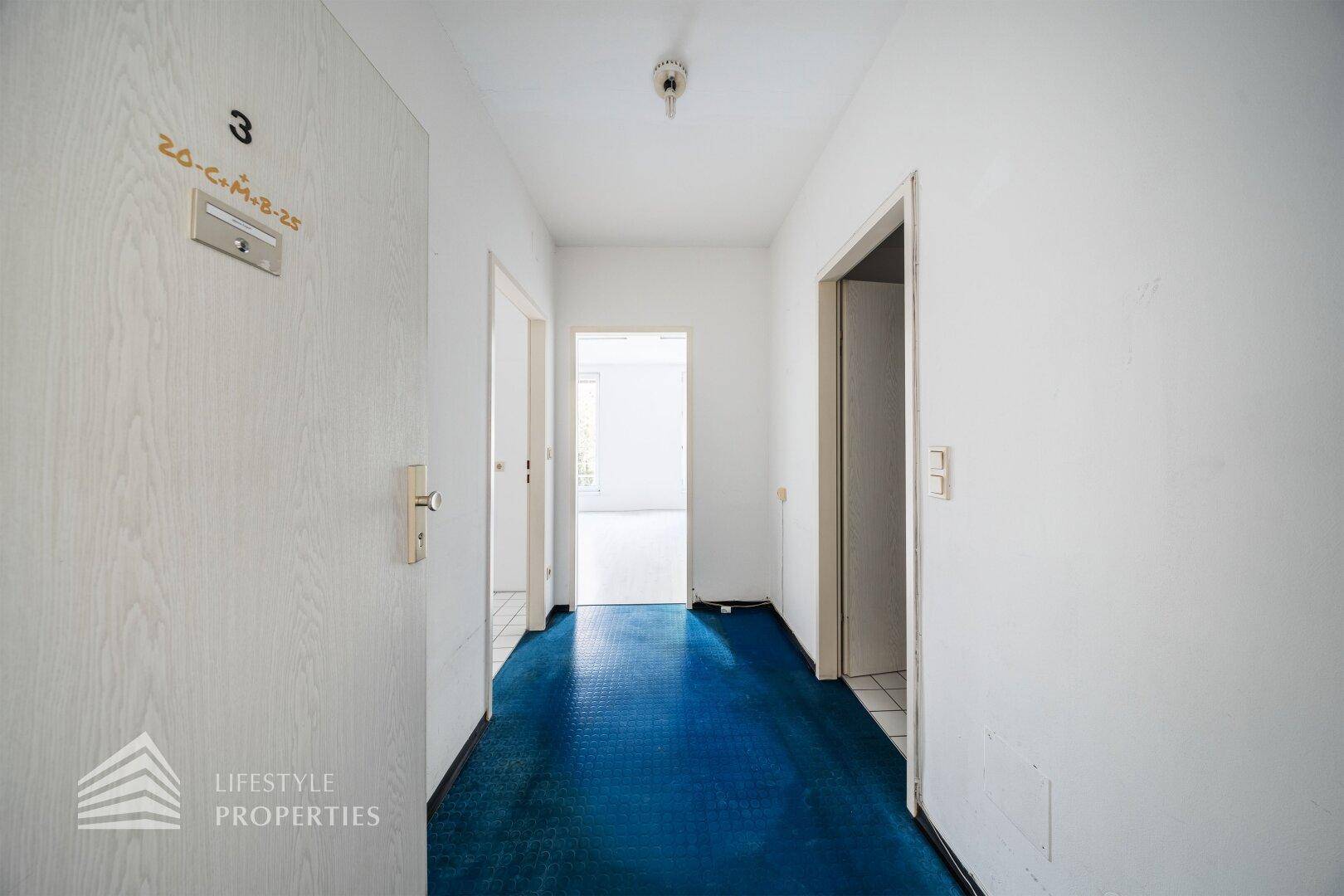 Langer Flur mit blauem Teppichboden und mehreren Türen zu den angrenzenden Räumen.
