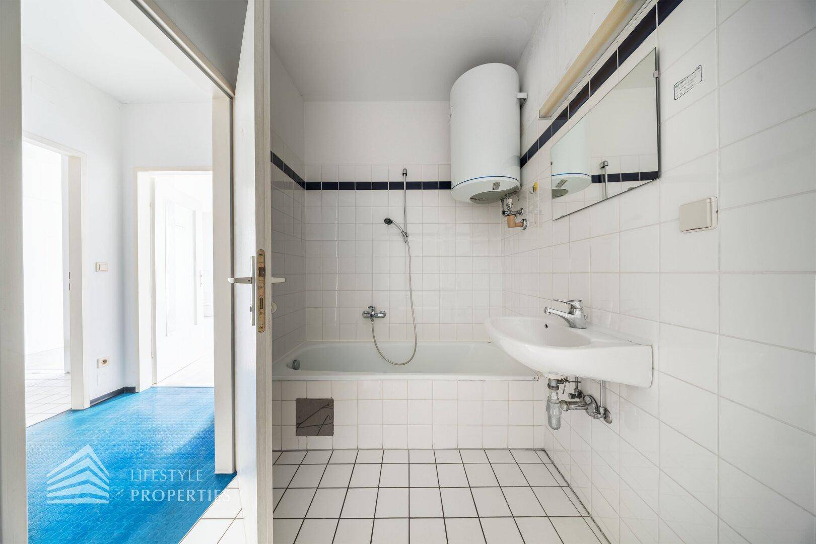 Badezimmer mit Badewanne, Waschbecken und weißen Fliesen, ausgestattet mit einem Boiler.