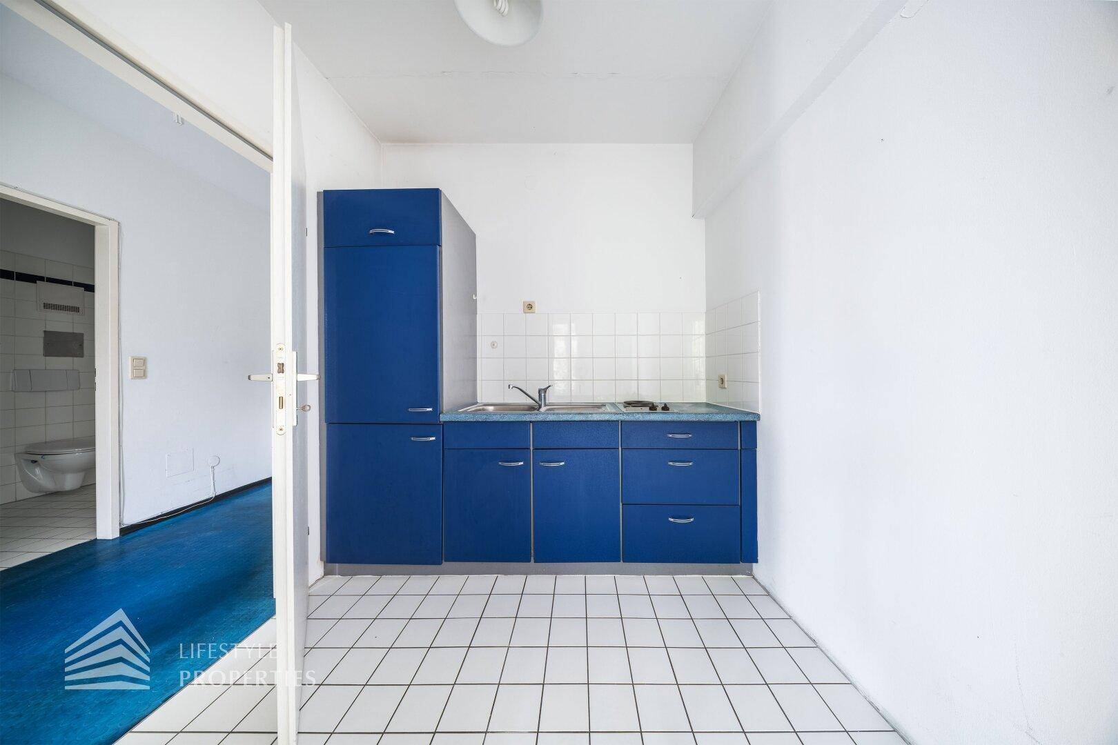 Einfache Küche mit blauen Unterschränken, Spüle und Herd, bereit zur Modernisierung.
