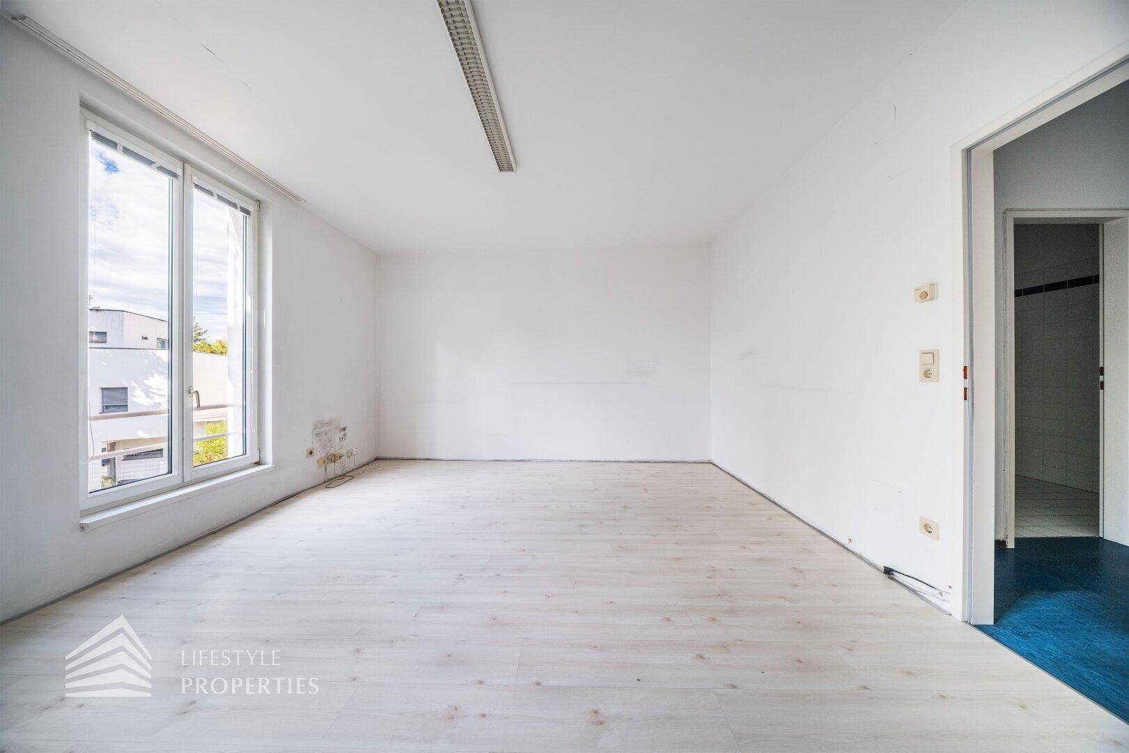 Leeres Zimmer mit großen Fenstern und hellem Laminatboden, ideal für verschiedene Nutzungsmöglichkeiten.